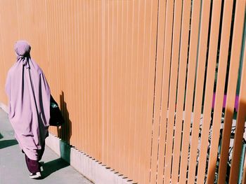 Full length rear view of woman walking by orange fence during sunny day