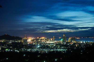 Illuminated city against cloudy sky at night