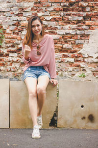 Portrait of mid adult woman sitting against brick wall