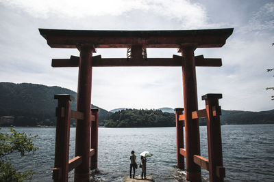 People standing by lake against sky