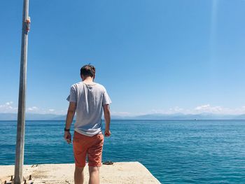 Rear view of man standing by sea against blue sky