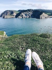 Low section of person on rock by sea against sky