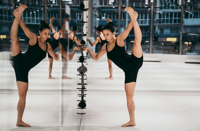 Full length of woman stretching while standing by mirror at gym