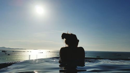 Rear view of silhouette woman swimming in infinity pool by sea during sunny day