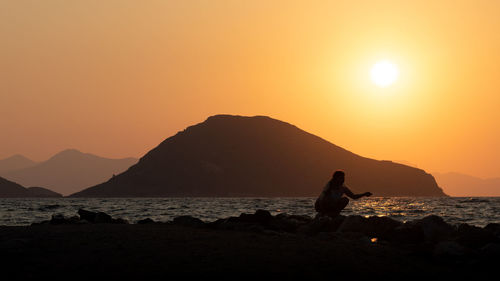 Silhouette man on rock by sea against sky during sunset