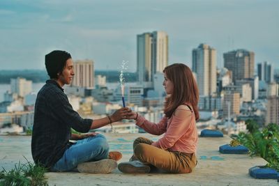 Young couple sitting in city against sky