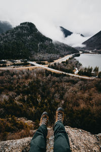 Low section of person on cliff in front of lake and mountains