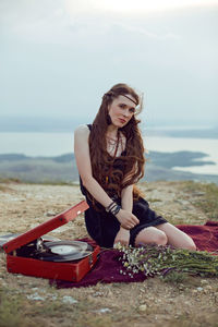 Young woman lies in nature in a black dress next to an old gramophone and listens to music