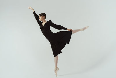 A ballerina in a black dress sexually demonstrates stretching  by performing an arabesque