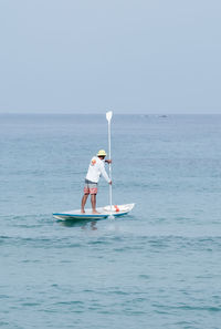 Man paddleboarding in sea against clear sky