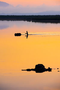 Silhouette man in lake against sky during sunset