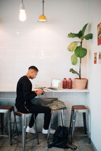 Full length of young male blogger sitting with camera and laptop at cafe