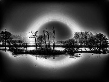 Silhouette bare trees by lake against sky during winter