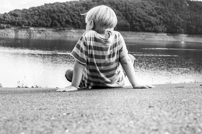 Rear view of boy sitting by lake