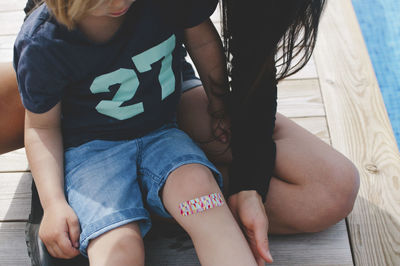 Boy wearing bandage sitting with mother at yard