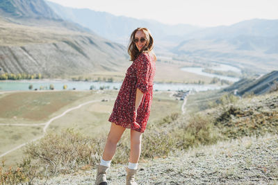 Young brunette woman in red dress on background of turquoise katun river, altai mountains