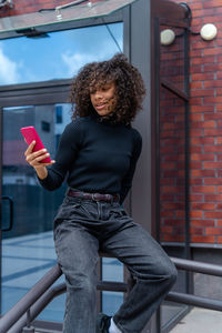 Pretty girl with curly hair using mobile phone in the city. female blogger using smart phone