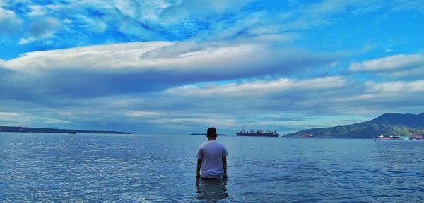 Rear view of man standing in sea against sky