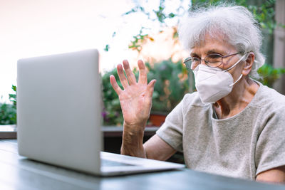 Elderly woman with face mask using laptop to chat via internet