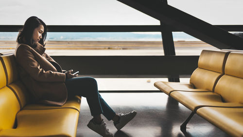 Woman using mobile phone while sitting on chair at airport