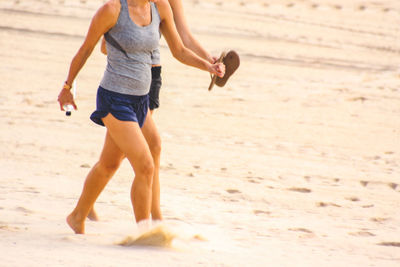 Low section of female friends walking at sandy beach