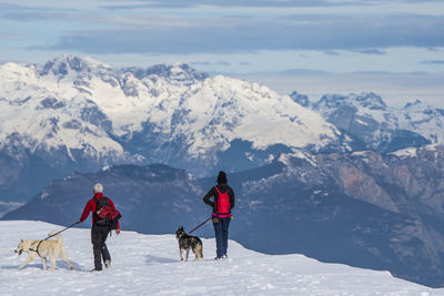 People with dogs walking on snowcapped mountains during winter
