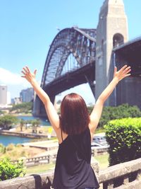 Rear view of woman with arms outstretched standing against sydney harbour bridge