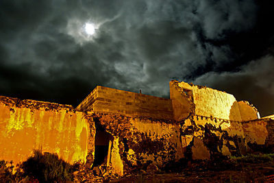 Low angle view of illuminated lighting equipment against dramatic sky