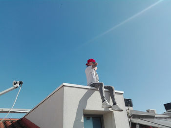 Low angle view of man working on building against clear blue sky