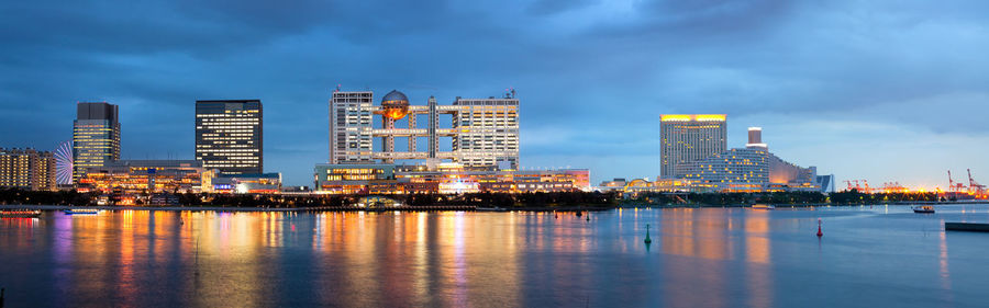 Illuminated city by river against sky