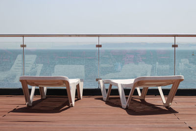 Deck chairs in ship against railing in front of sea