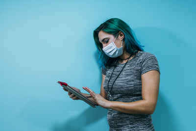 Young woman using phone while standing against blue wall