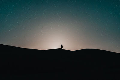 Silhouette man standing on mountain against sky at night