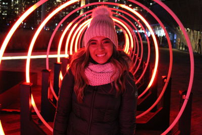 Portrait of smiling woman against illuminated built structure at night