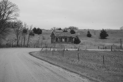 Dirt road by farm against sky