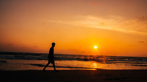 Silhouette man on beach against sky during sunset
