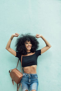 Happy woman with curly hair standing against wall