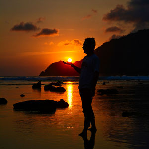 Silhouette man standing on beach against sky during sunset