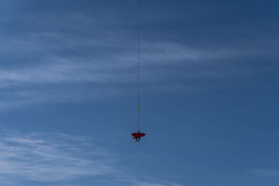 Low angle view of person hanging on rope against blue sky