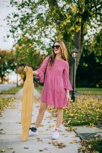 Girl smiling wearing sunglasses standing on sidewalk holding a skateboard