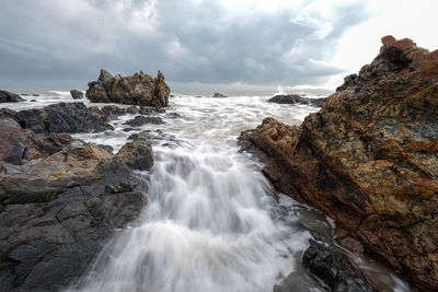 Long exposure image of waves crashing at beach against storm clouds