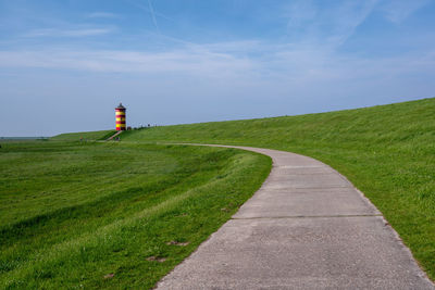 Road leading towards lighthouse on field against sky