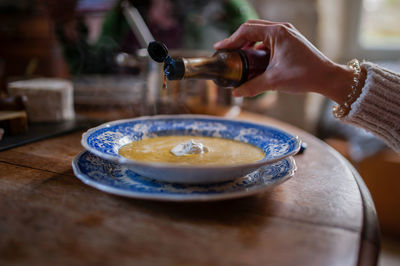 Cropped image of person pouring sauce into soup on table