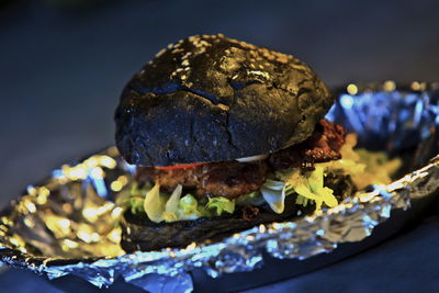 Close-up of black bun burger on foil in plate