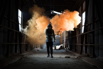 Full length of man holding distress flare while walking in abandoned workshop