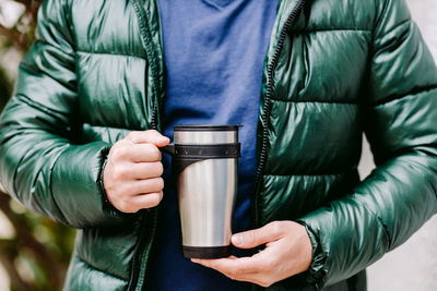 Midsection of man holding coffee mug wile standing outdoors