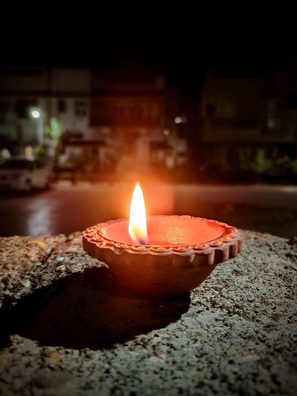 CLOSE-UP OF LIT CANDLE ON RETAINING WALL