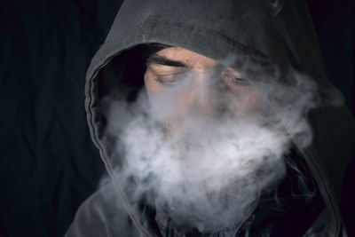 Man wearing hood clothing while smoking in darkroom