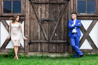 Full length portrait of a young woman standing against wooden wall