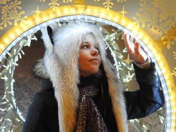 Close-up of smiling girl wearing warm clothing while touching illuminated lighting equipment